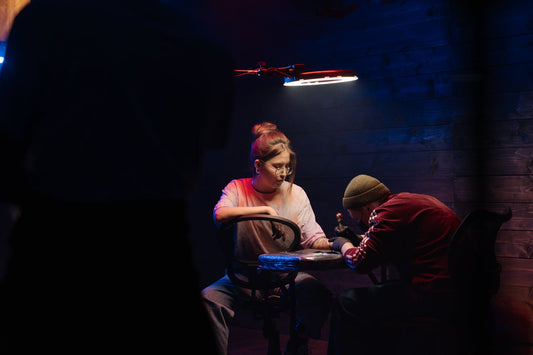 Un tatoueur tatoue une femme dans une pièce sombre à la lumière tamisée.